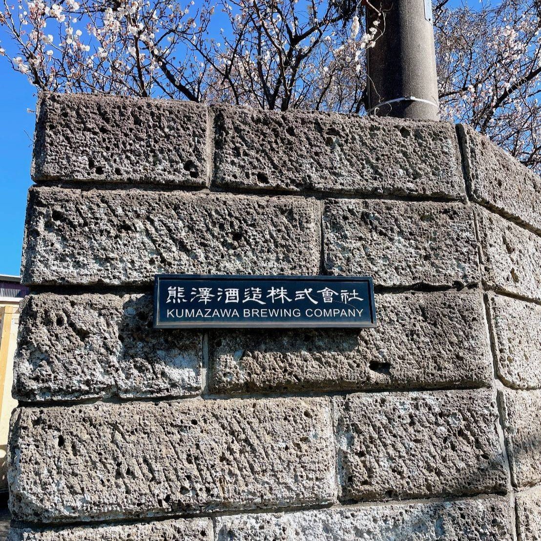 石積みの門柱に掛かる「熊澤酒造株式會社」の銘板。背景に梅の花