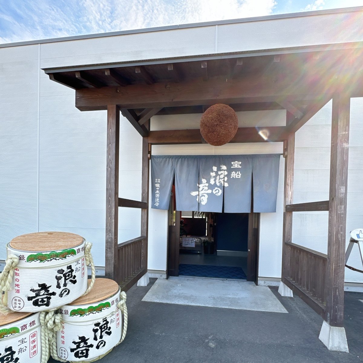 杉玉が下がる蔵の入口。「宝船 浪の音」ののれんと、手前に菰樽が積まれている